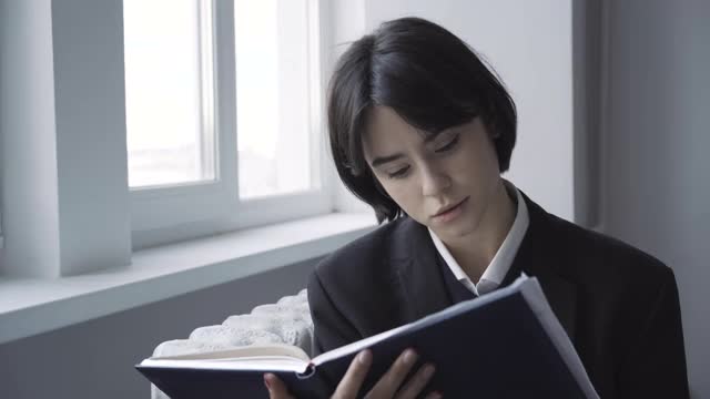 深色头发的白人少女在走廊里看书。聪明有思想的公立学校学生享受假期的肖像。教育和智力观念。视频素材