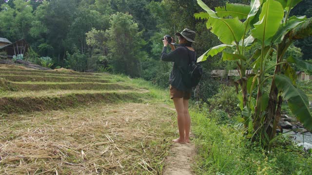 亚洲女性在乡村旅行中用相机拍照，以山和森林为背景的风景。自然旅行的概念。4 k慢动作。视频素材