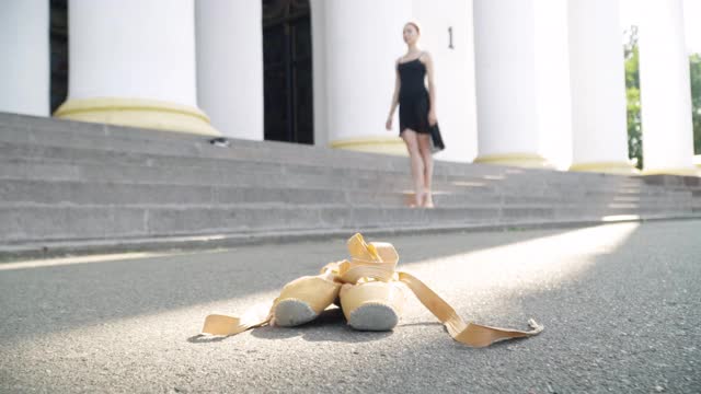 脚尖鞋躺在阳光下，苗条的白人芭蕾舞女演员在背景上跳舞。宽阔的镜头，不认识的年轻女子在户外表演交际舞在阳光明媚的夏天的一天。视频素材