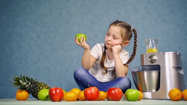 漂亮的小女孩坐在桌子上吃苹果。有趣的孩子坐在有机水果，咬苹果和喝新鲜果汁。视频素材