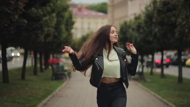 一位年轻女子边走边戴着耳机听着音乐。她在跳舞和唱歌。4 k。视频素材