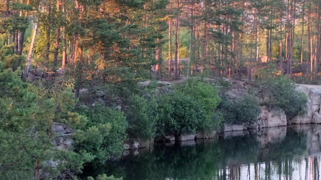 全景式的美丽清澈的湖之间的花岗岩和松树林反映在水在日落在夏季，阳光照耀透过树木，4k视频素材