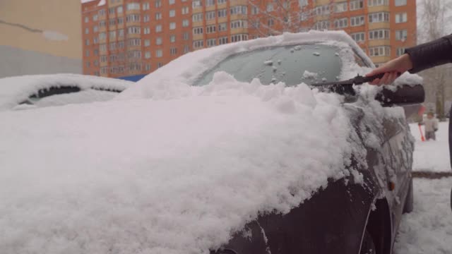 一名妇女在暴风雪后用刷子清理汽车。视频素材