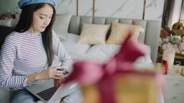 女人在家里收到了一份圣诞礼物。兴奋的女人拿着圣诞礼物。亚洲妇女倒数并通过视频电话会议庆祝新年派对。视频素材