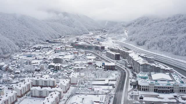 鸟瞰图的冬季村庄Krasnaya Polyana度假村被白雪覆盖的山脉包围。从直升机上拍摄高山奥林匹克谷与建设基础设施的现代旅游场所视频素材