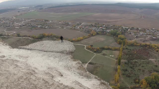 鸟瞰图男性获胜者站在白岩的顶峰，享受成功，思考自然景观。活跃的男子从悬崖顶上欣赏山谷，庆祝战胜4k乡村视频素材