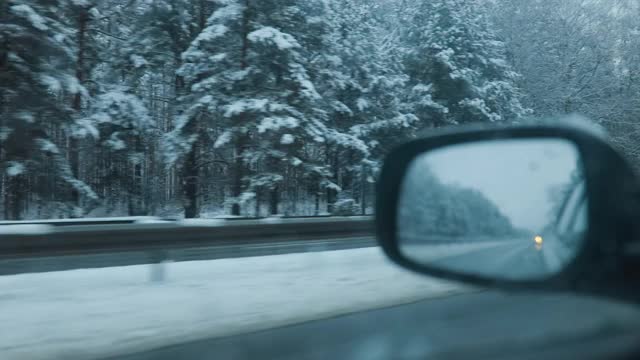 内景的汽车镜和人驾驶在冬天的高速公路上与雪在树上视频素材