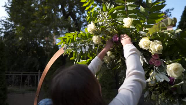 员工活动机构工作。花商装裱，装饰花拱为婚礼。工作创造的婚礼装饰专业。植物种类。装饰师用鲜花构成婚礼拱门视频素材