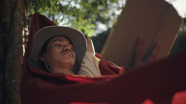 一个年轻人躺在吊床上看书视频素材