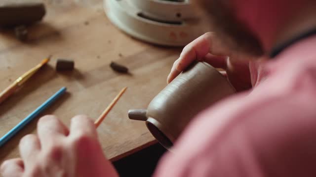 职业男工匠陶工在手工陶壶上塑造壶嘴。陶瓷艺术的概念。手工制作的陶器。陶工制作粘土制品视频素材