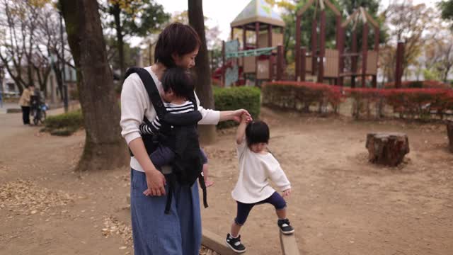 小女孩在妈妈的帮助下在公园的平衡木上行走-第二部分视频素材