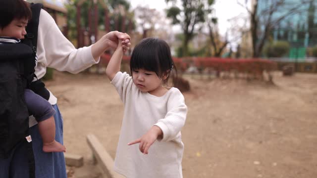 小女孩在妈妈的帮助下在公园的平衡木上行走-第二部分视频素材