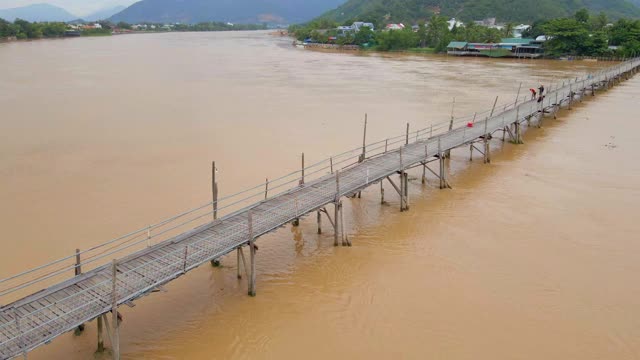 空中慢镜头拍摄的木桥横跨亚洲的河流和摩托车骑在上面。危险交通建设概念视频素材