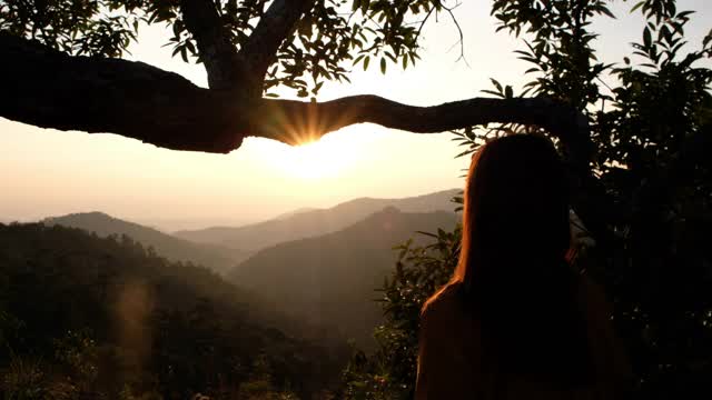 一个女性旅行者的后视镜形象站在山顶和看日出在早上视频素材