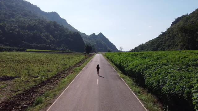 一名妇女在乡村山路上行走的无人机鸟瞰图视频素材