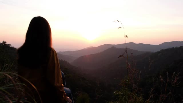 模糊的一个女旅人坐在山顶上，在早晨看日出视频素材