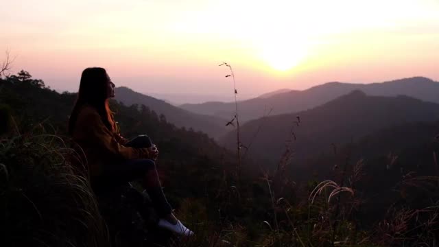 模糊的一个女旅人坐在山顶上，在早晨看日出视频素材