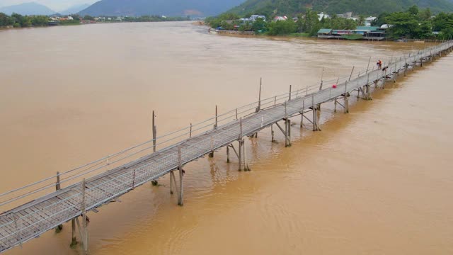 空中慢镜头拍摄的木桥横跨亚洲的河流和摩托车骑在上面。危险交通建设概念视频素材