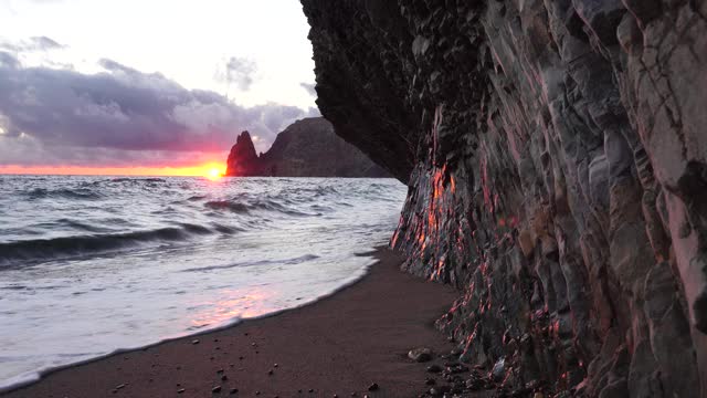 彩色温暖的日落在海上和火山玄武岩，就像在冰岛。海浪撞击着岩石，在温暖的夕阳照耀下溅起白色的泡沫。大自然永无止境的美丽视频素材