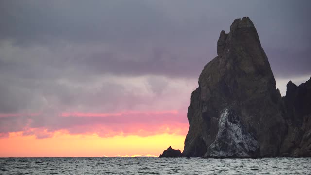 彩色温暖的日落在海上和火山玄武岩，就像在冰岛。海浪撞击着岩石，在温暖的夕阳照耀下溅起白色的泡沫。大自然永无止境的美丽视频素材