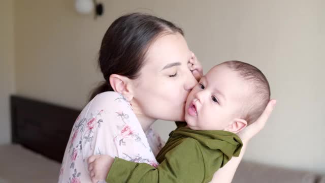 妈妈亲吻刚出生的儿子抱在怀里在家里玩耍。母亲节，幸福家庭理念视频素材