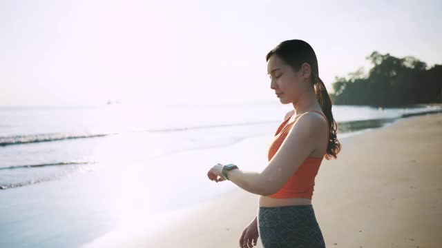 亚洲运动女性使用智能手表监测她在海滩上的跑步表现视频素材