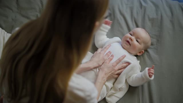 美丽的微笑宝宝:一个漂亮的小婴儿躺在床上，对着镜头微笑，背景是一个很好的软焦视频素材