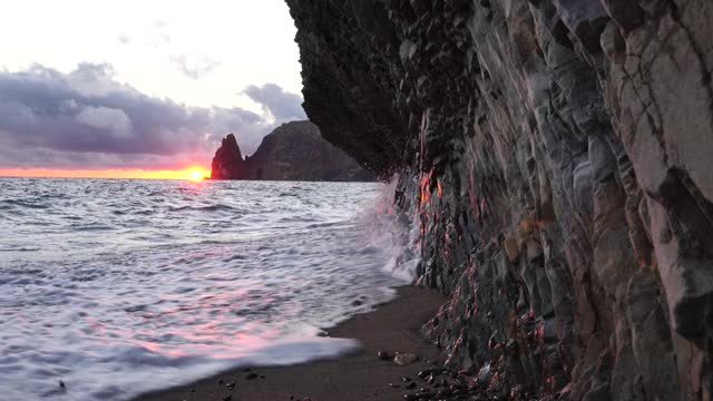 彩色温暖的日落在海上和火山玄武岩，就像在冰岛。海浪撞击着岩石，在温暖的夕阳照耀下溅起白色的泡沫。大自然永无止境的美丽视频素材