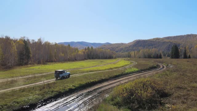 一辆汽车在田野周围的乡村道路上行驶，森林的背景是一座山，直升机在拍摄视频素材