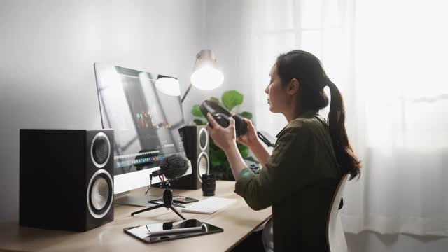 亚洲女性摄像师在写字台上做视频和音频编辑的电影镜头女性内容创作者使用专业设备现代技术网络无线处理电影蒙太奇。,放大视频素材