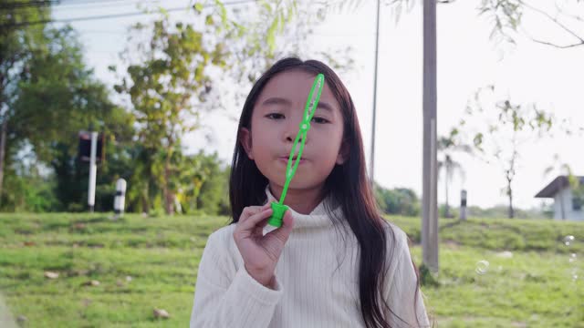 一个小女孩吹肥皂泡有乐趣，享受在阳光明媚的周末。视频素材