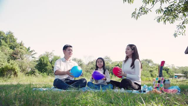 幸福的家庭野餐。亚洲父母(父亲，母亲)和女儿玩玩具飞机，在绿色的花园野餐布上享受我们自己在阳光明媚的一天视频素材