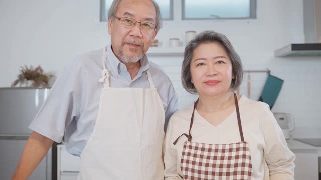 夫妇老亚洲长者幸福生活在家庭厨房。爷爷抱着奶奶幸福地笑着一起享受退休生活。老年人的家庭关系和活动概念。视频素材