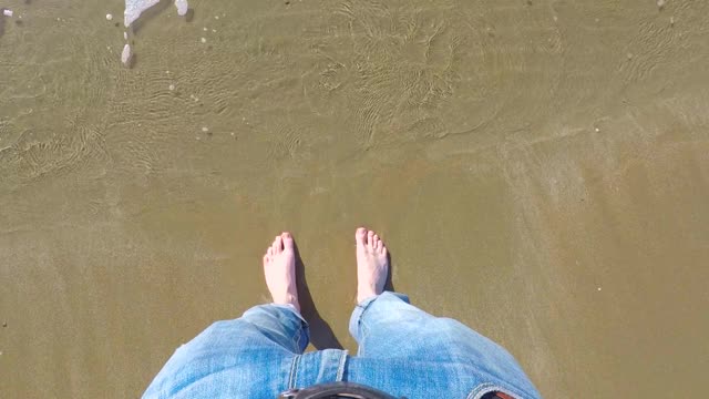 穿着牛仔裤的男人在沙滩上踏着海浪在沙水里视频素材