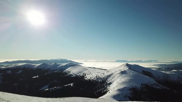 在Amerinkogel地区，一架无人机拍摄到被雪覆盖的阿尔卑斯山。山谷里有浓雾。山坡上茂密的森林。奥地利阿尔卑斯山的冬天。无尽的山脉。阳光明媚的一天。视频素材