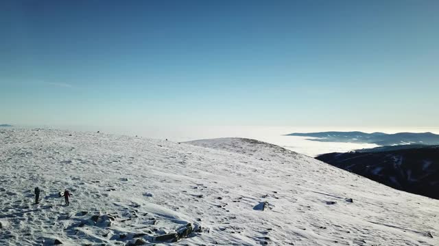 无人机拍摄到一对夫妇穿着雪地鞋徒步前往Amerinkogel峰。奥地利阿尔卑斯山的冬天。无尽的山脉，覆盖着新鲜的粉末雪。阳光明媚的一天。冬季户外活动视频素材