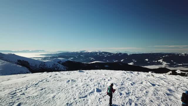 无人机拍摄到一对夫妇穿着雪地鞋徒步前往Amerinkogel峰。奥地利阿尔卑斯山的冬天。无尽的山脉，覆盖着新鲜的粉末雪。阳光明媚的一天。冬季户外活动视频素材