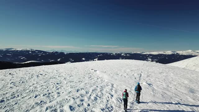 无人机拍摄到一对夫妇穿着雪地鞋徒步前往Amerinkogel峰。奥地利阿尔卑斯山的冬天。无尽的山脉，覆盖着新鲜的粉末雪。阳光明媚的一天。冬季户外活动视频素材