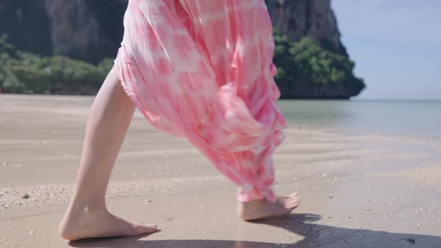 下半身女性穿着粉色沙滩装跑进热带岛屿海滩的海洋中，海水在慢动作中溅起水花。暑假旅游目的地人间天堂，乐趣和快乐视频素材