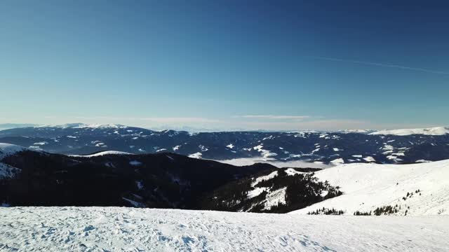 在Amerinkogel地区，一架无人机拍摄到被雪覆盖的阿尔卑斯山。山谷里有浓雾。山坡上茂密的森林。奥地利阿尔卑斯山的冬天。无尽的山脉。阳光明媚的一天。视频素材