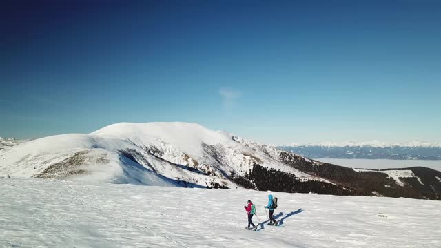 无人机拍摄到一对夫妇穿着雪地鞋徒步前往Amerinkogel峰。奥地利阿尔卑斯山的冬天。无尽的山脉，覆盖着新鲜的粉末雪。阳光明媚的一天。冬季户外活动视频素材