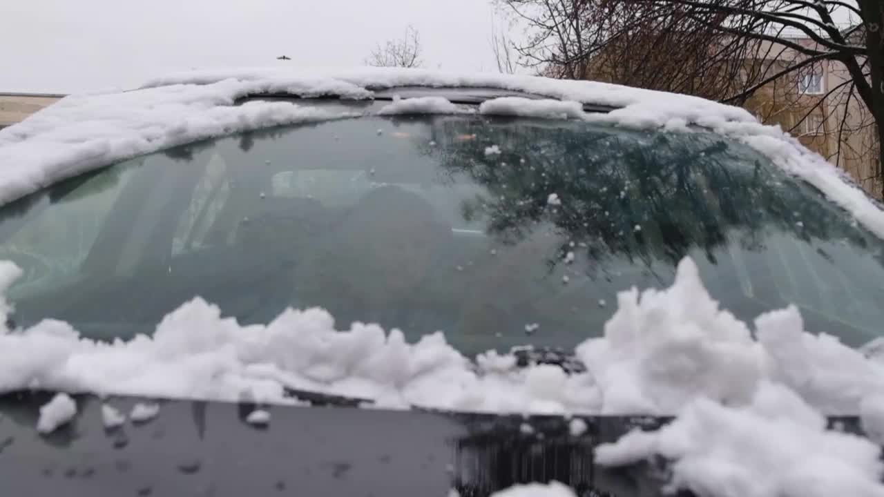 司机把车从房子附近的雪中挖了出来。刮车挡风玻璃上的雪和冰。一位妇女用刷子清理车上的雪视频素材