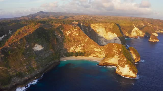 在印尼克林金海滩的悬崖、蓝色海浪和金色海滩的无人机视图。旅游天堂目的地景观靠近巴厘岛。田园诗般的沙滩和大浪。视频素材