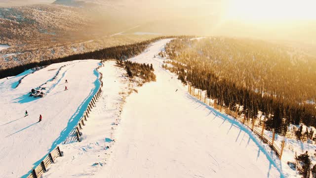 从鸟瞰图上可以看到日落时滑雪场的斜坡和斜坡，滑雪者和滑雪板爱好者沿着跑道滚向令人惊叹的日落视频素材