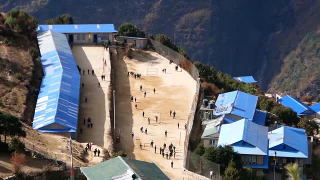 尼泊尔喜马拉雅山昆布Namche Bazar的蓝色波纹铁皮屋顶学校鸟瞰图，孩子们在操场上玩耍。视频素材