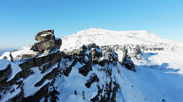 在一个阳光明媚的冬日，壮观的无人机沿着积雪覆盖的岩石山峰飞行视频素材