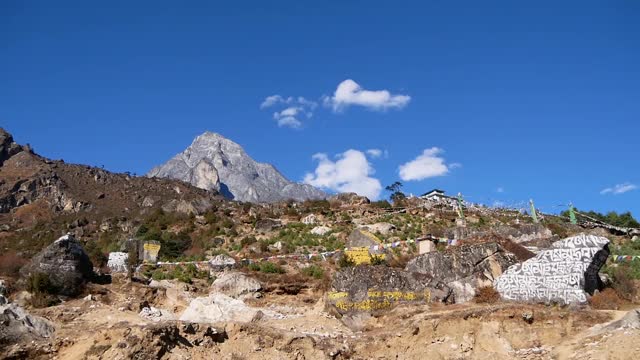 尼泊尔喜马拉雅山脉昆布地区夏尔巴人村庄Namche Bazar上方的斜坡上，彩色的佛教经幡在强风中飘扬，mani石头。视频素材