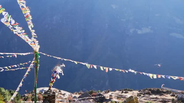 尼泊尔夏尔巴人村庄Namche Bazar上空，五颜六色的佛教经幡在强风中飘扬，直升飞机降落，扬起尘土。视频素材