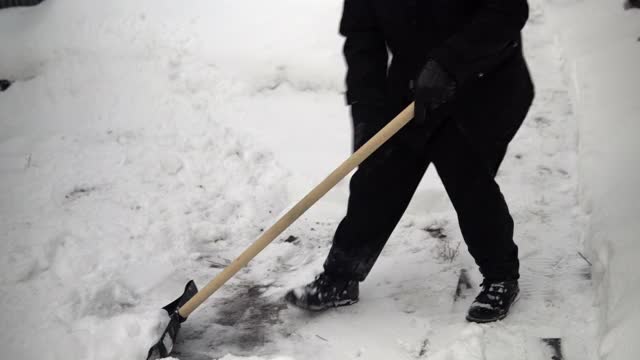 一个穿黑衣服的人用铲子在他的院子里清理雪。俄罗斯的冬天把院子覆盖上了雪视频素材