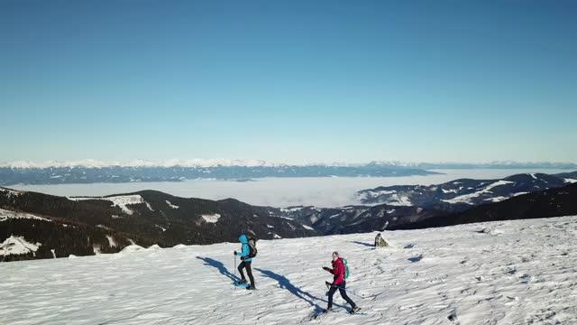 无人机拍摄到一对夫妇穿着雪地鞋徒步前往Amerinkogel峰。奥地利阿尔卑斯山的冬天。无尽的山脉，覆盖着新鲜的粉末雪。阳光明媚的一天。冬季户外活动视频素材